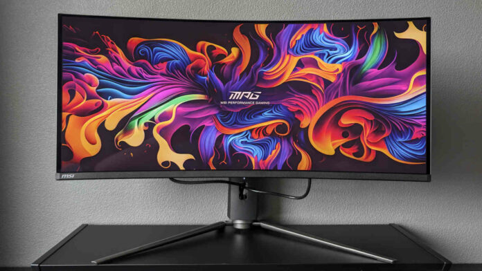 MSI MPG 341CQPX QD-OLED standing atop a black surface, against a grey background, its display brightly lit by ribbons of various colours