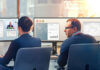 Two colleagues sitting next to each other in front of business monitors.