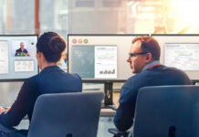 Two colleagues sitting next to each other in front of business monitors.