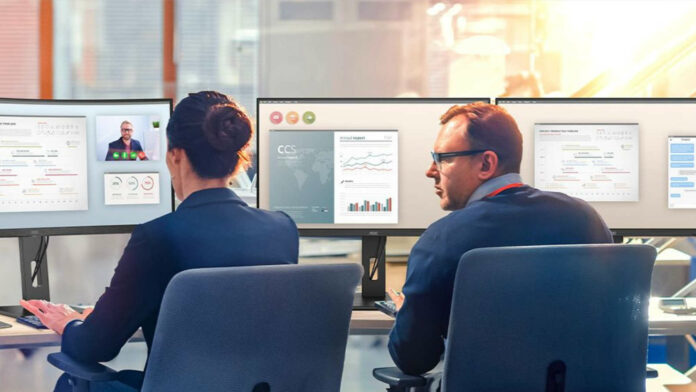 Two colleagues sitting next to each other in front of business monitors.