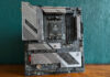 ASRock X870E Taichi Lite motherboard, standing upright on a wooden surface, against a green background.