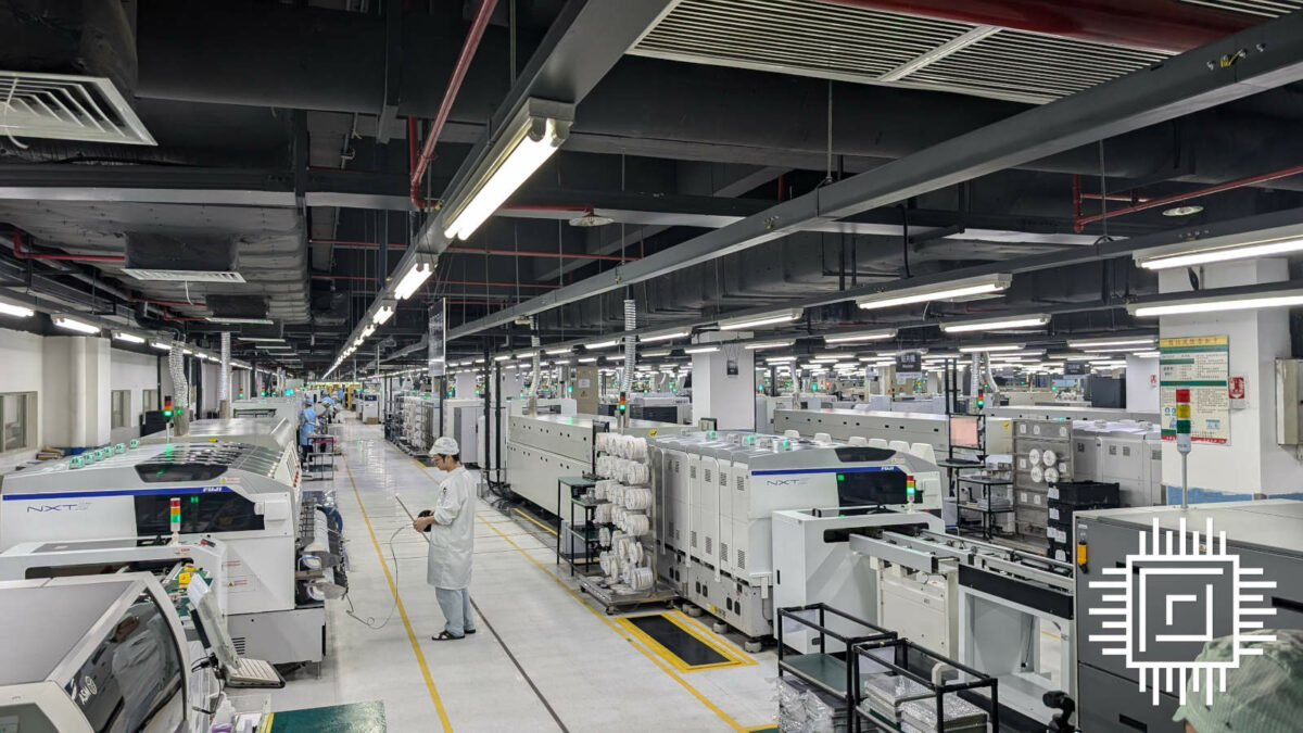 Wide shot of a factory floor, made of up white machines and floors, with few operators walking along its halls.