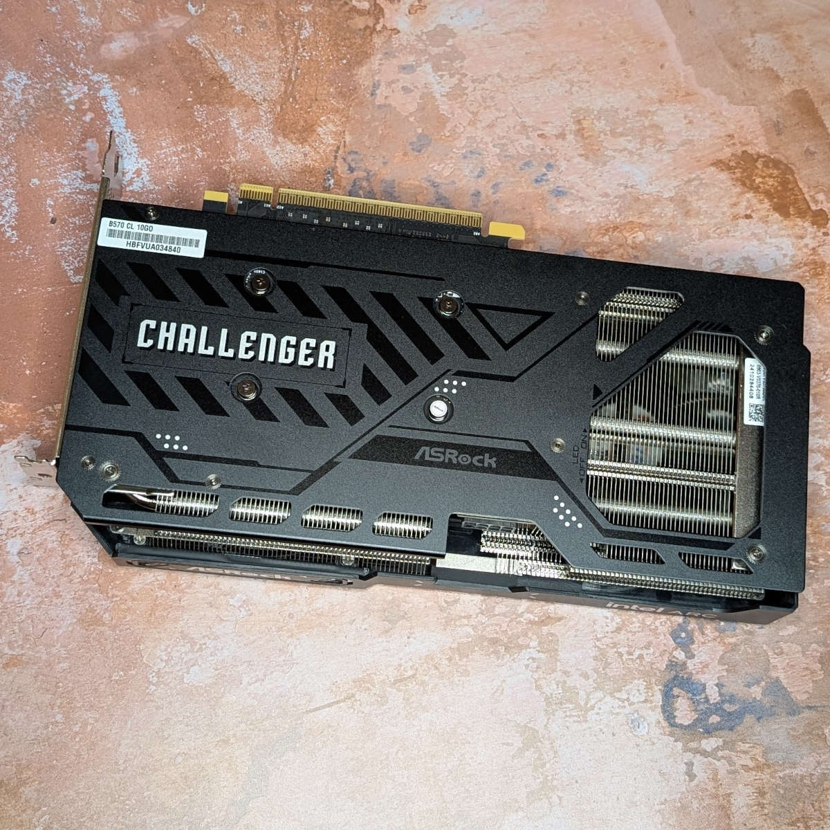 Rear view of ASRock Challenger OC Arc B570 graphics card, against an orange backdrop.